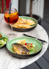 Food on the table summer terrace, grilled sea bass fillet and hummus.