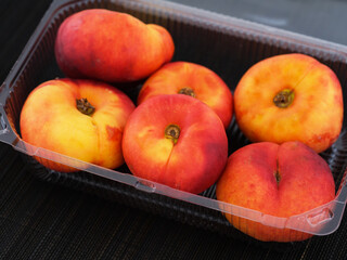 Plastic container with ripe flat peaches in it on black bamboo napkin