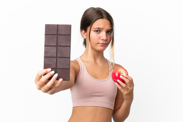 Little caucasian girl isolated on white background taking a chocolate tablet in one hand and an...