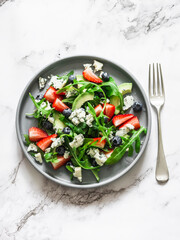 Arugula, strawberry, gorgonzola, avocado salad on a light background, top view