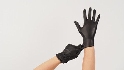 Hands is pulling black latex gloves on white background.