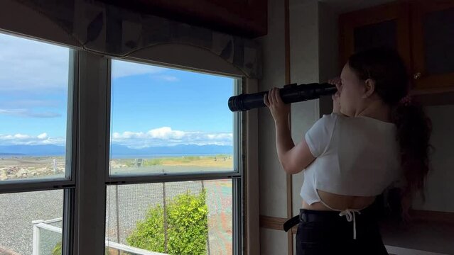 a teenager A girl stands in the trailer room and looks through a spyglass at the Pacific Ocean, looking for animals, the sea or ships, she is alone and bored but interesting Parksville beach