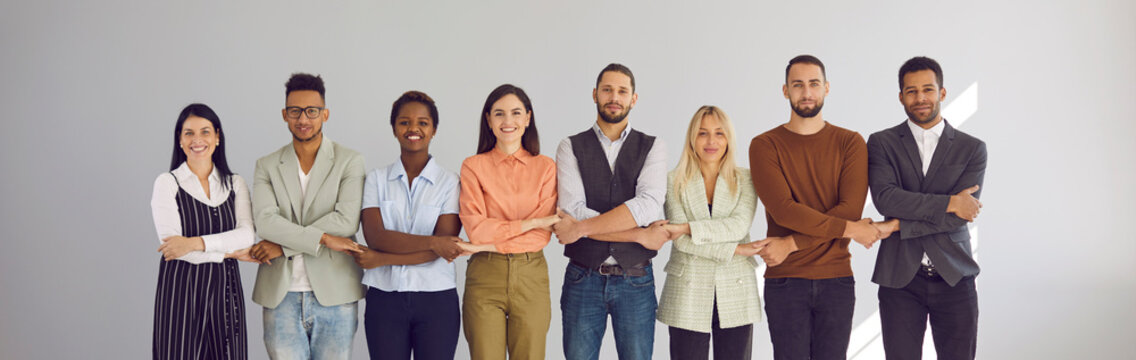 Portrait of successful group of business people standing together in row and holding hands. Multiracial people on light background. Concept of strong community, mutual assistance and support. Banner.