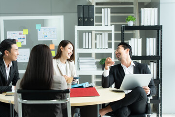 A group of young Asian entrepreneurs. Top Management is meeting to review stock investment data from the team in a meeting room with natural light