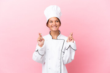 Little caucasian chef girl isolated on pink background with fingers crossing