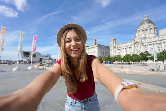 Tourism in Liverpool, UK. Beautiful young woman takes selfie picture in front of Pier Head with "The Three Graces" in the city centre of Liverpool, England.