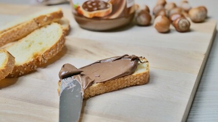 a knife applies chocolate and hazelnut cream on a slice of freshly baked bread, close-up. increase home cooked breakfast