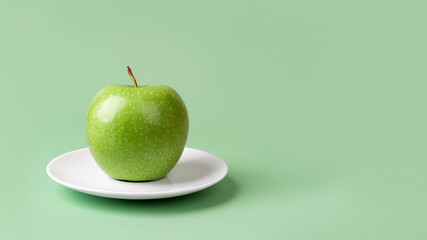 Fresh green apple on a white saucer over pastel green background. Organic ingredient for slimming diet. Weight loss healthy eating. Vitamin vegetarian fruit snack. Copy space.