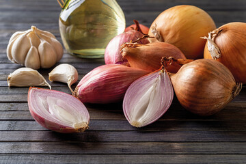 Fresh red shallot, yellow onion and garlic on a black wooden background. Whole and halved long...