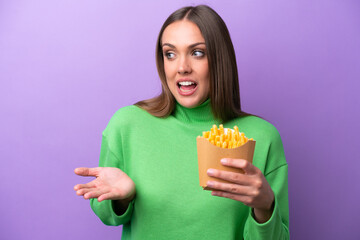 Young caucasian woman holding fried chips on purple background with surprise expression while looking side