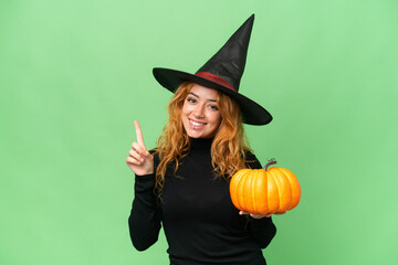 Young caucasian woman costume as witch holding a pumpkin isolated on green screen chroma key background showing and lifting a finger in sign of the best