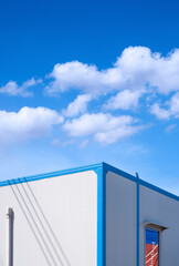 Perspective side view of white office container in commercial dock area against cloud on blue sky in vertical frame 