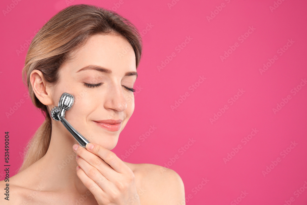 Canvas Prints Young woman using metal face roller on pink background, space for text