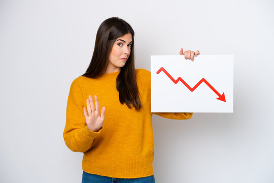 Young Brazilian woman isolated on white background holding a sign with a decreasing statistics arrow symbol and doing stop sign