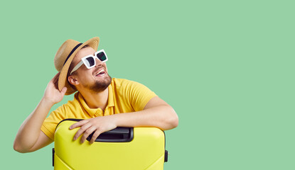 Wide narrow shot of funny smiling young man in summer hat and sunglasses with suitcases dream of vacation or trip. Happy male traveler imagine good holidays. Copy space. Travel and tourism concept. - obrazy, fototapety, plakaty