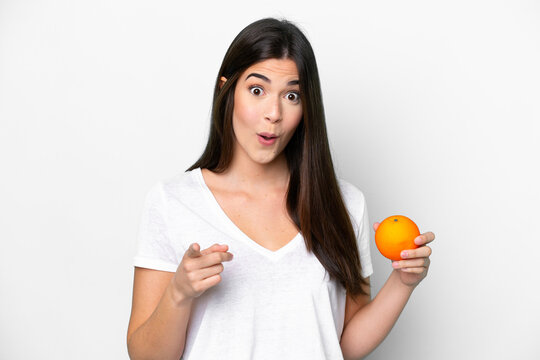 Young Brazilian woman holding an orange isolated on white background surprised and pointing front