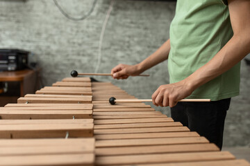 Hands of a young musician playing sticks on a wooden musical instrument xylophone, close-up, selective focus