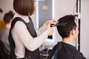 Asian woman hairstylist using scissors and comb for hair cut and design on man's hair in barbershop.