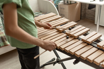 Hands of a young musician playing sticks on a wooden musical instrument xylophone, close-up,...