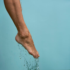 Close up of a female wet foot with water gliding over it on a blue background