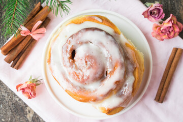 Homemade Cinnabon Buns with Cinnamon and Cream on white plate on wooden table and napkin. Wooden background. Selective focus