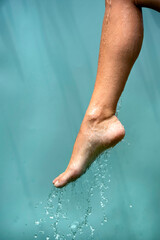 Close up of a female wet foot with water gliding over it on a blue background