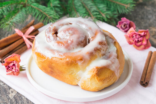 Homemade Cinnabon Buns with Cinnamon and Cream on white plate on wooden table and napkin. Wooden background. Selective focus