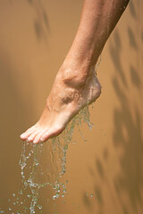 Close up of a female wet foot with water gliding over it on a beige background,