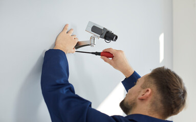 Fototapeta premium Technician worker install security camera on wall in office or home for indoors safety. Male electrician mount surveillance CCTV system for crime or bribe detection. Modern technology concept.