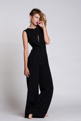 Fototapeta premium Fashion photo of a beautiful elegant model posing in the Studio. Black jumpsuit. White, soft gray background. Studio Shot. Portrait