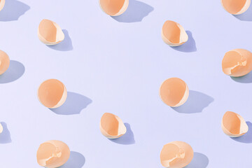 Abstract kitchen texture made with broken hen egg shells on isolated pastel purple background with copy space. Minimal cooking ingredient or healthy food concept. Sun and shadows. Easter card pattern.