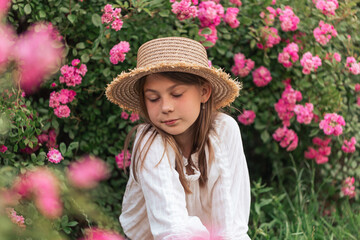 Cute little girl with blond hair in a straw hat. Pink flowers. Summer.