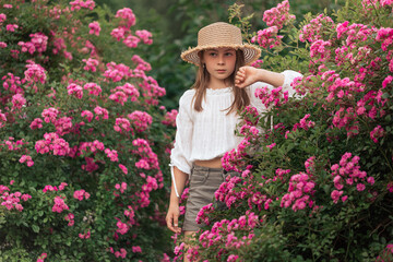 Cute little girl with blond hair in a straw hat. Pink flowers. Summer.