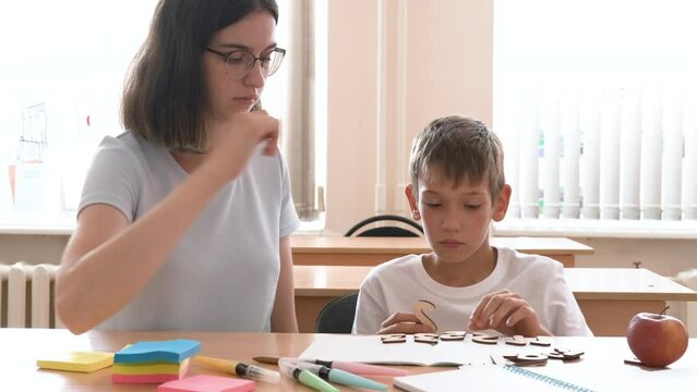 The child and the teacher do math, lay out wooden numbers on the table. A mother helps her son learn to count. The babysitter helps to complete school assignments. back to school