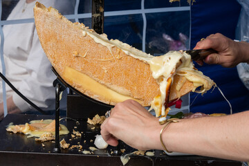 A delicious wheel of raclette cheese has been heated on the cutting edge so that it is in a molten...