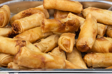 A bowl of delicious tasty spring rolls sit on the counter of a fast food street vendor waiting to be served to hungry customers looking for southheast asian flavors and spices