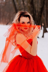 Beautiful woman in a luxurious red fairy-tale dress in a snowy forest