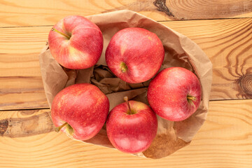 Several sweet red apples with paper bag on wooden table, macro, top view.
