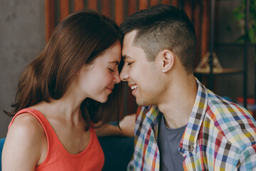 Close up young couple two friends family man woman in casual clothes pressing their foreheads sits on blue sofa together stay at home flat rest spend free spare time in living room indoors grey wall.