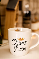 A white cup with the inscription Queen Mama stands on the table in the kitchen