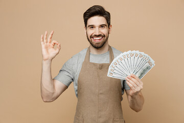 Young man barista barman employee in brown apron work in coffee shop hold fan of cash money in...