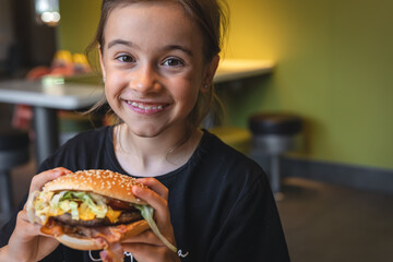 A little girl eats an appetizing burger, close-up.