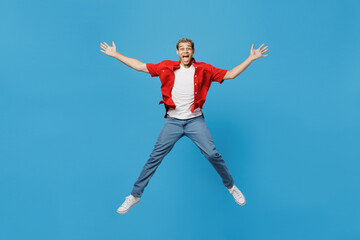 Fototapeta na wymiar Full size young fun excited man of African American ethnicity 20s wear red shirt jump high with outstretched hands legs isolated on plain pastel light blue cyan background. People lifestyle concept