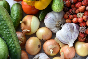 Vegetables and berries close-up. Strawberries onions cucumbers and garlic in a pile of autumn harvest.