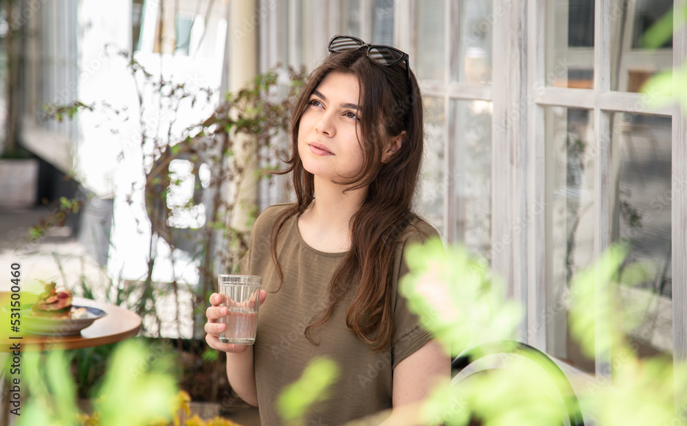 Poster attractive young woman with a glass of water on a summer day on a cafe terrace.