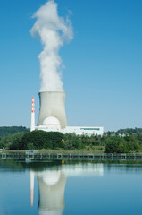 Nuclear power plant on the Rhine river bank. Leibstadt, Switzerland  
Smoke is rising from the cooling tower. It reflects on the water.