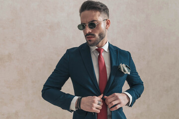 sexy young guy with sunglasses adjusting and opening navy blue suit