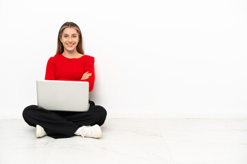 Young caucasian woman with a laptop sitting on the floor keeping the arms crossed in frontal...