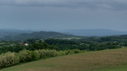 Naklejka premium HIlly village with scattered houses and mountain in haze during gloomy day, rural landscape