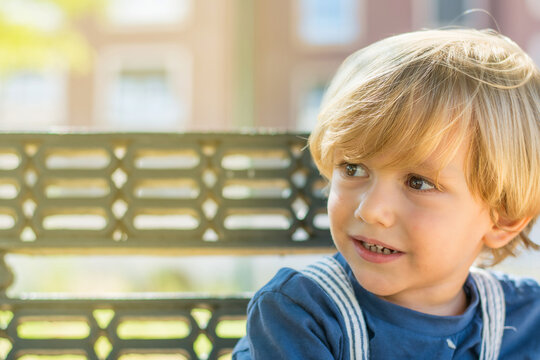 Portrait of a 2 year old blond boy with an out of focus background in a park. Close-up of adorable little boy's face smiling. Image with copy space